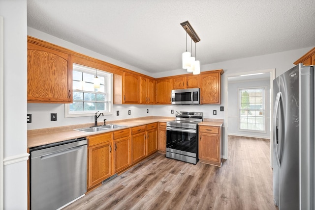 kitchen featuring sink, light hardwood / wood-style flooring, appliances with stainless steel finishes, hanging light fixtures, and a textured ceiling