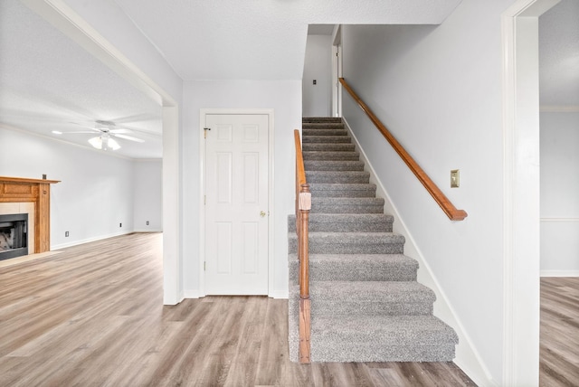 stairway featuring hardwood / wood-style flooring, ceiling fan, ornamental molding, and a textured ceiling