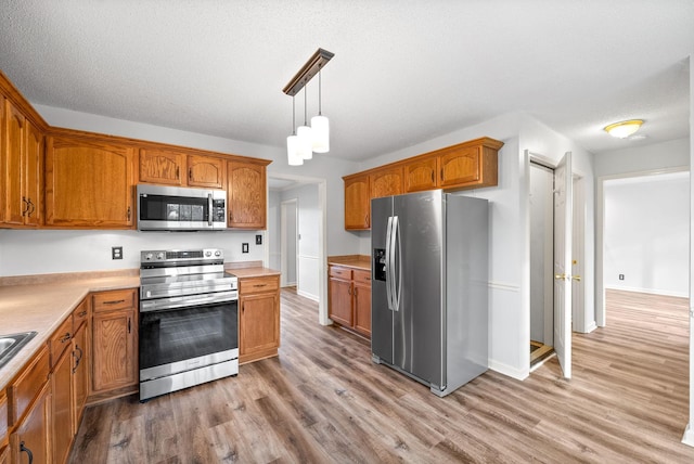 kitchen featuring stainless steel appliances, hanging light fixtures, a textured ceiling, and light hardwood / wood-style floors