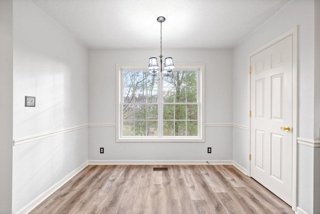 unfurnished dining area with an inviting chandelier, a textured ceiling, and light wood-type flooring