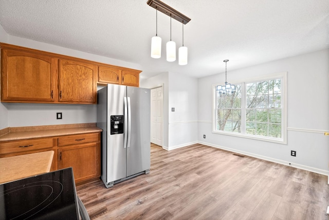 kitchen with stainless steel refrigerator with ice dispenser, an inviting chandelier, decorative light fixtures, light wood-type flooring, and range with electric cooktop