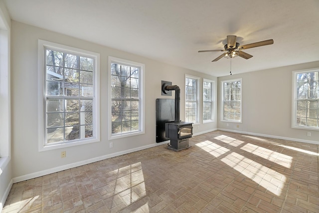 unfurnished living room with ceiling fan and a wood stove