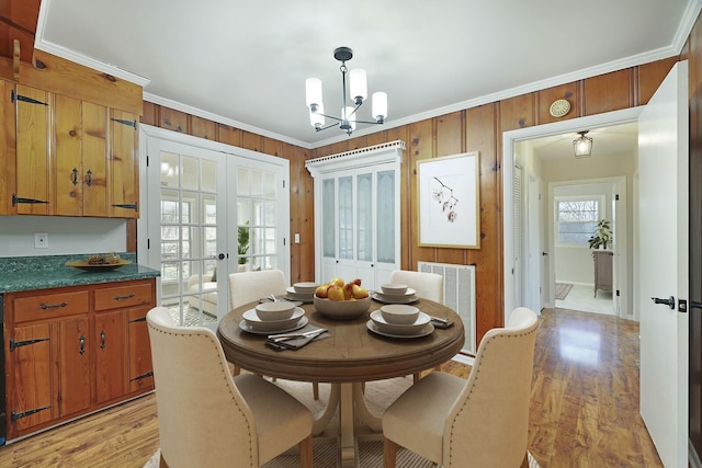 dining space with french doors, crown molding, an inviting chandelier, light wood-type flooring, and wooden walls