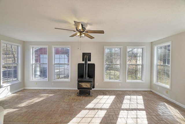 unfurnished living room with a wood stove and ceiling fan