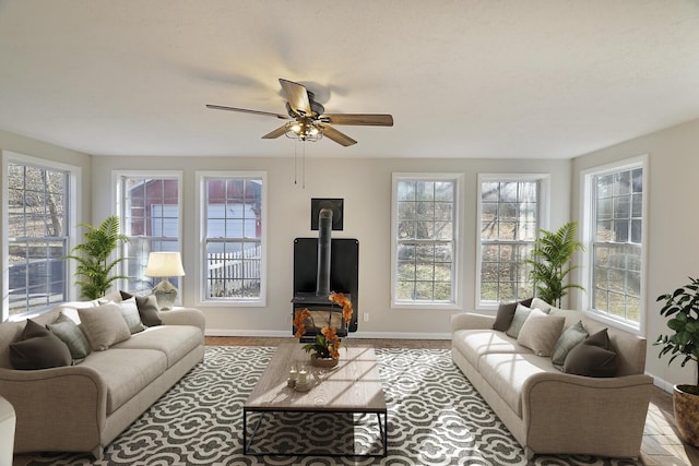 living room with a healthy amount of sunlight, a wood stove, and ceiling fan