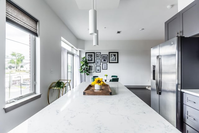 kitchen with stainless steel refrigerator with ice dispenser, decorative light fixtures, light stone countertops, and a wealth of natural light