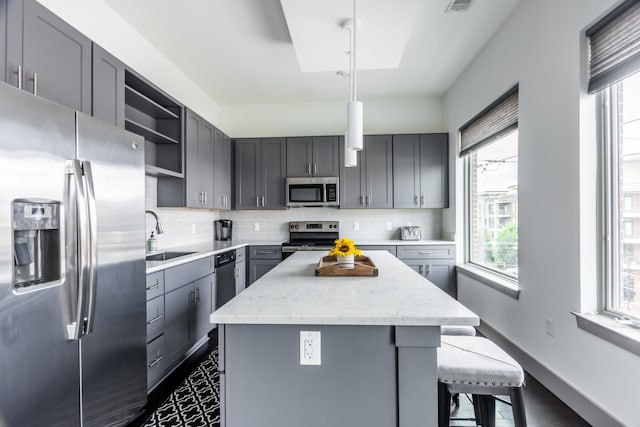 kitchen with gray cabinetry, hanging light fixtures, sink, and appliances with stainless steel finishes