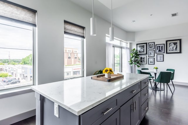 kitchen with pendant lighting, dark wood-type flooring, gray cabinetry, light stone countertops, and a kitchen island