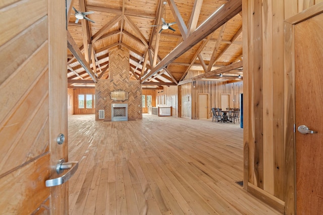 unfurnished living room with wood ceiling, ceiling fan, high vaulted ceiling, beamed ceiling, and wood walls