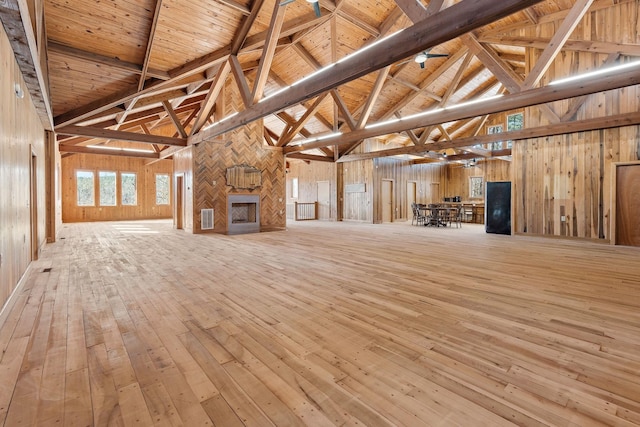 unfurnished living room featuring beam ceiling, wood ceiling, high vaulted ceiling, a fireplace, and light hardwood / wood-style floors