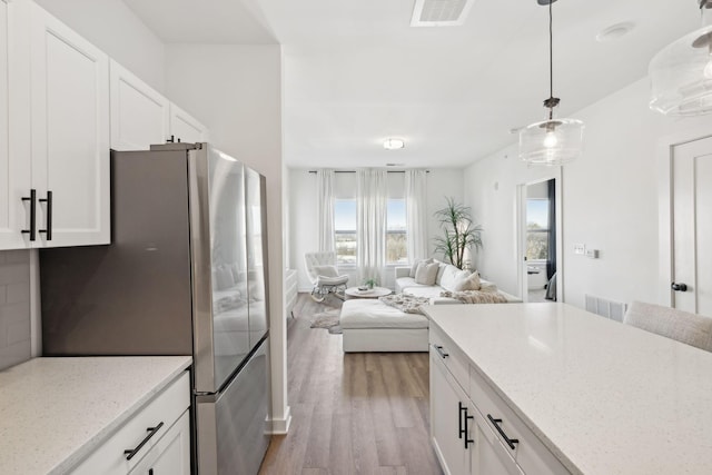 kitchen with stainless steel refrigerator, light stone countertops, hanging light fixtures, and white cabinets