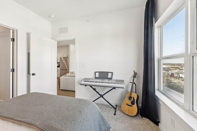 bedroom featuring multiple windows, light colored carpet, and stainless steel fridge