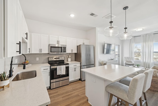 kitchen featuring sink, appliances with stainless steel finishes, backsplash, white cabinets, and decorative light fixtures