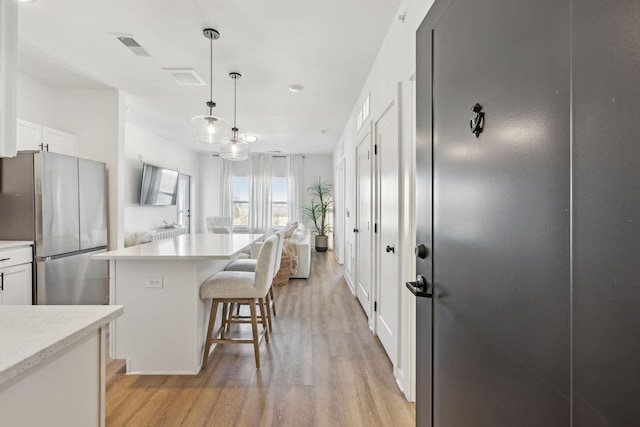 kitchen featuring white cabinetry, pendant lighting, stainless steel fridge, and a kitchen island