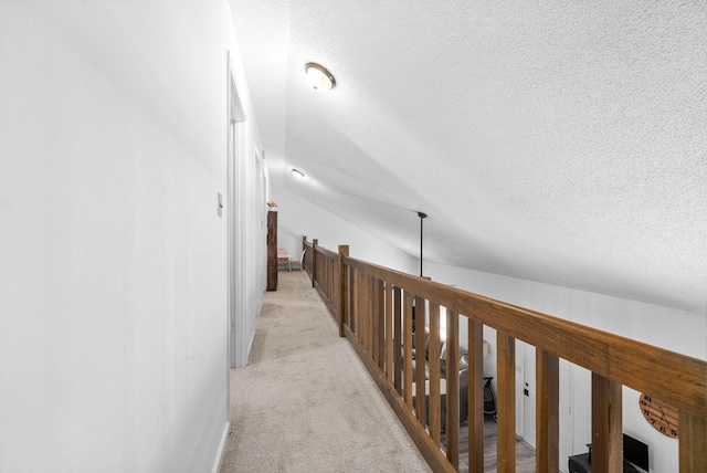 hallway featuring lofted ceiling, light colored carpet, and a textured ceiling