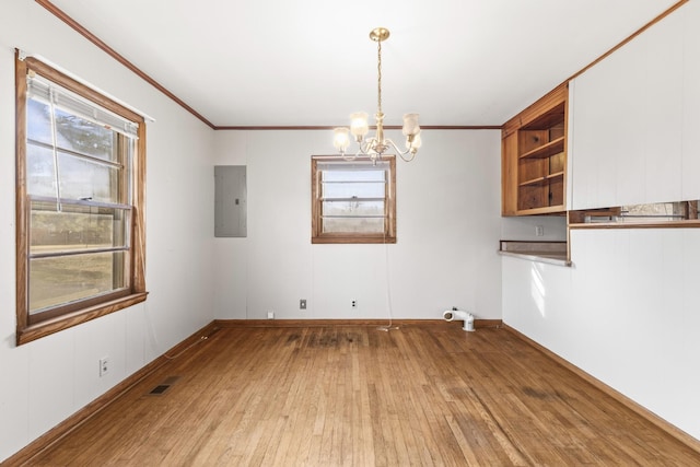 unfurnished dining area with an inviting chandelier, crown molding, electric panel, and light wood-type flooring