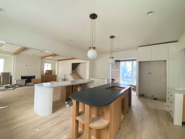 kitchen with white cabinetry, pendant lighting, light hardwood / wood-style floors, and a center island with sink