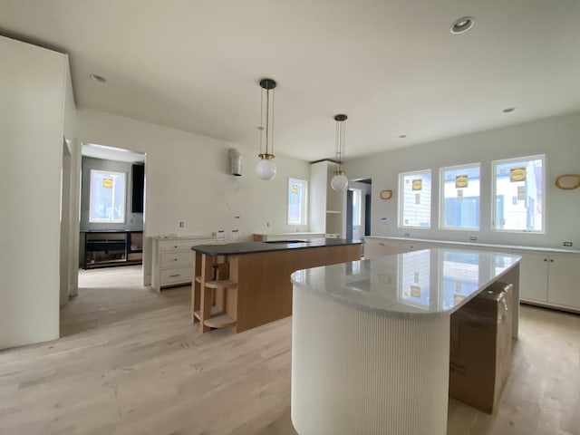 kitchen with hanging light fixtures, a center island, white cabinets, and light wood-type flooring