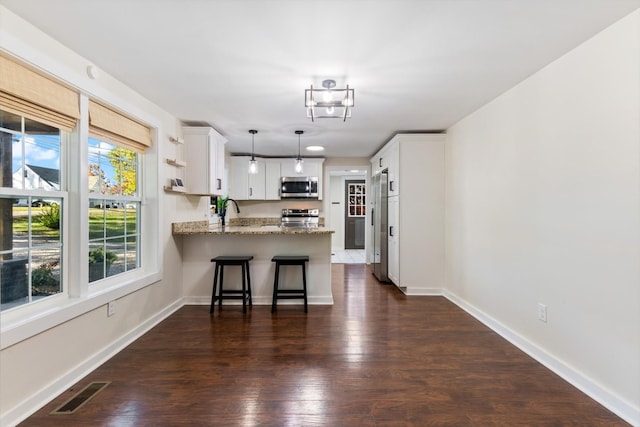 kitchen with appliances with stainless steel finishes, white cabinetry, hanging light fixtures, light stone counters, and kitchen peninsula