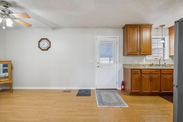 kitchen with pendant lighting, sink, light hardwood / wood-style floors, a healthy amount of sunlight, and a textured ceiling