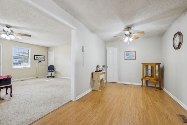 living area with a textured ceiling, ceiling fan, and light hardwood / wood-style floors