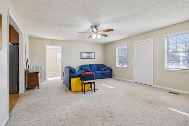 living room featuring ceiling fan, light carpet, and a textured ceiling