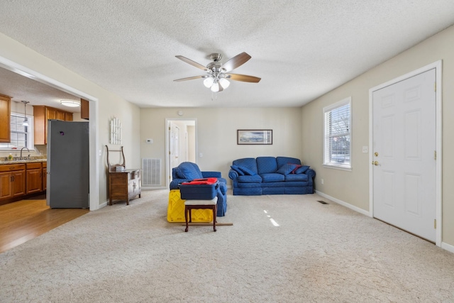 carpeted living room featuring ceiling fan, a healthy amount of sunlight, sink, and a textured ceiling