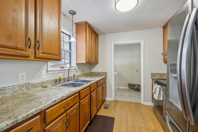 kitchen featuring decorative light fixtures, sink, light hardwood / wood-style floors, stainless steel appliances, and a textured ceiling