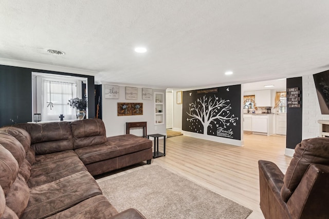 living room featuring built in shelves, light hardwood / wood-style flooring, and a textured ceiling