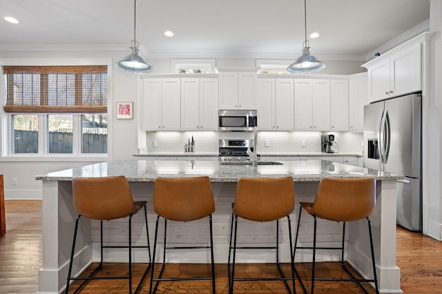 kitchen with white cabinetry, stainless steel appliances, decorative light fixtures, and an island with sink