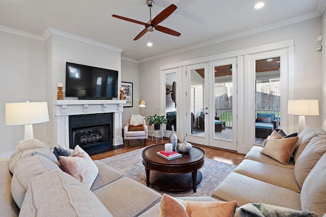 living room with crown molding, ceiling fan, a fireplace, wood-type flooring, and french doors