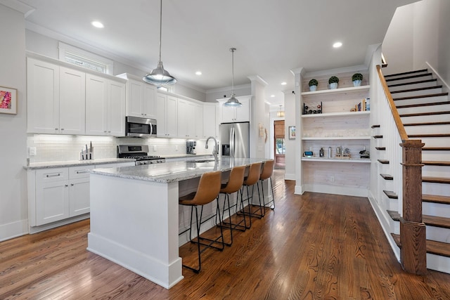 kitchen featuring white cabinetry, stainless steel appliances, an island with sink, and hanging light fixtures