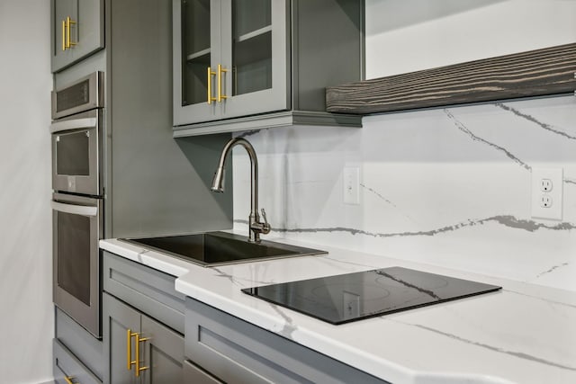 kitchen featuring sink, black electric cooktop, gray cabinets, stainless steel double oven, and light stone countertops