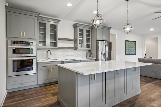 kitchen featuring sink, gray cabinetry, hanging light fixtures, light stone counters, and stainless steel appliances