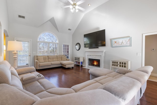 living room featuring dark wood-type flooring, ceiling fan, a fireplace, and high vaulted ceiling