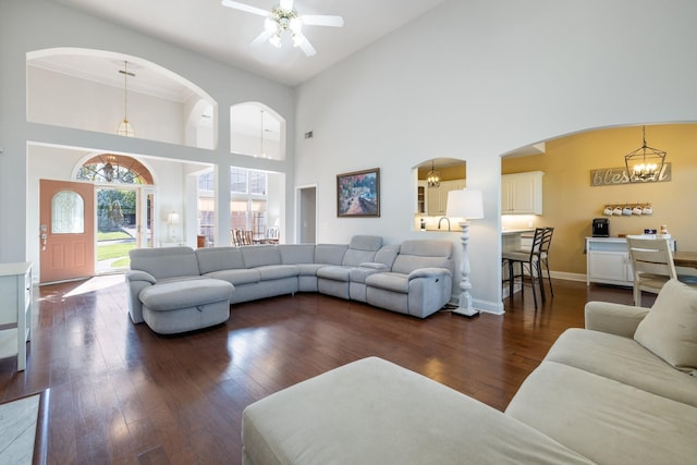 living room with a towering ceiling, ceiling fan with notable chandelier, and dark hardwood / wood-style floors