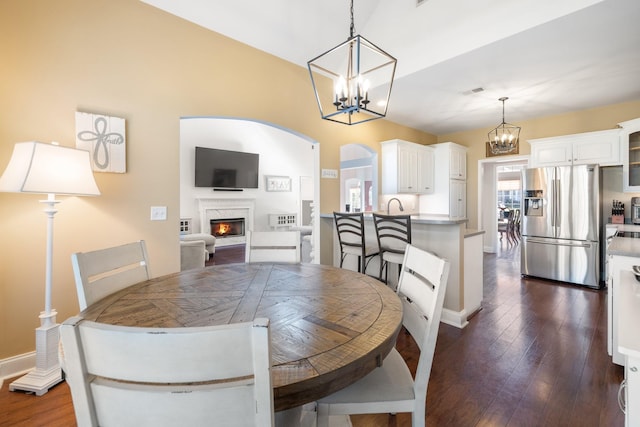 dining room with an inviting chandelier, dark hardwood / wood-style floors, vaulted ceiling, and a premium fireplace