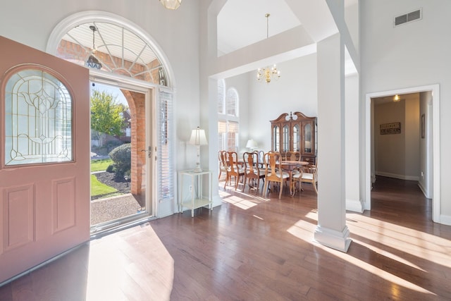 entrance foyer featuring an inviting chandelier, a towering ceiling, dark wood-type flooring, and ornate columns