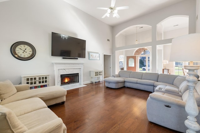 living room with a high end fireplace, dark wood-type flooring, ceiling fan, and a towering ceiling