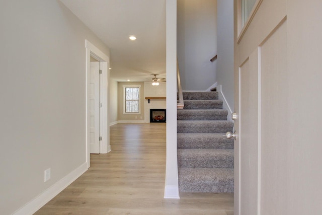 stairway featuring hardwood / wood-style flooring, a large fireplace, and ceiling fan