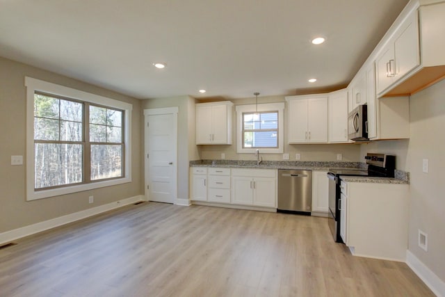 kitchen with white cabinetry, hanging light fixtures, appliances with stainless steel finishes, light stone countertops, and light hardwood / wood-style floors