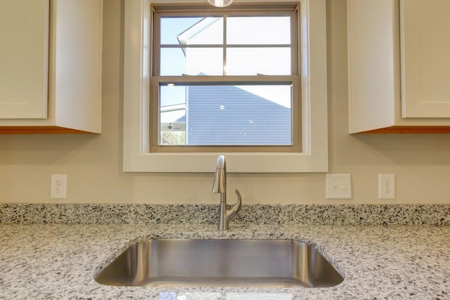 interior details featuring sink, light stone countertops, and white cabinets