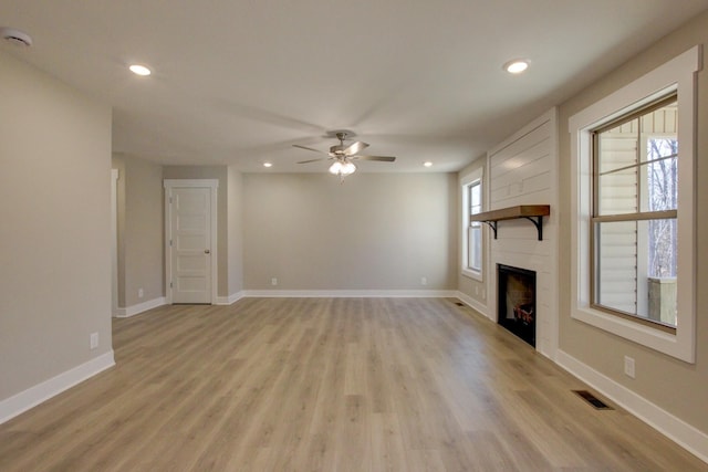 unfurnished living room with ceiling fan, a tiled fireplace, and light hardwood / wood-style flooring