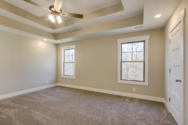 carpeted spare room featuring a raised ceiling, plenty of natural light, and ceiling fan