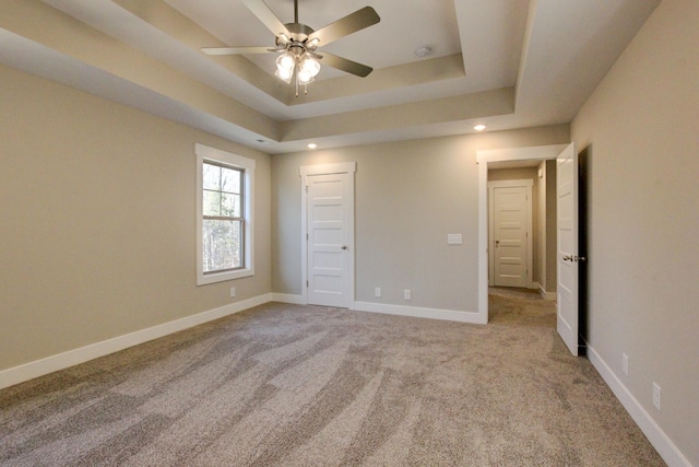 unfurnished bedroom featuring light colored carpet, ceiling fan, and a tray ceiling