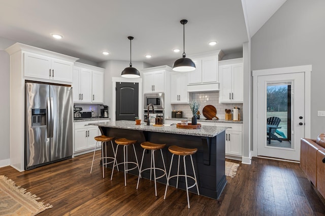 kitchen with white cabinetry, stainless steel appliances, a kitchen island with sink, and light stone counters