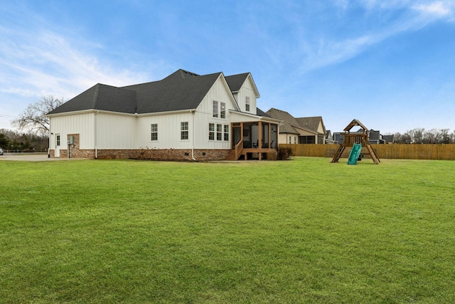 rear view of house with a playground, a sunroom, and a yard