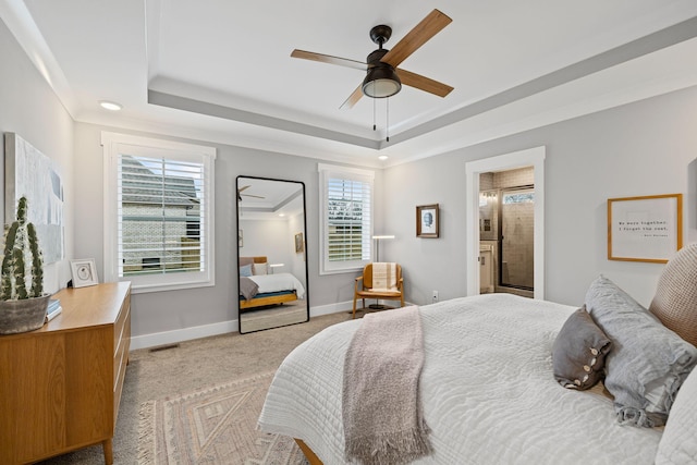 carpeted bedroom featuring ceiling fan, ensuite bathroom, a tray ceiling, and multiple windows