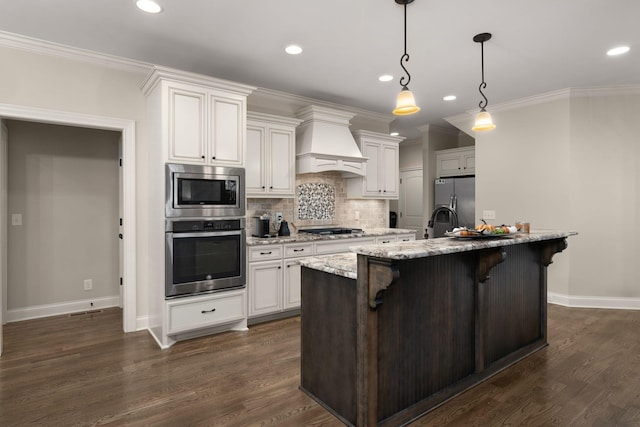 kitchen featuring a breakfast bar, decorative light fixtures, a center island with sink, appliances with stainless steel finishes, and custom range hood