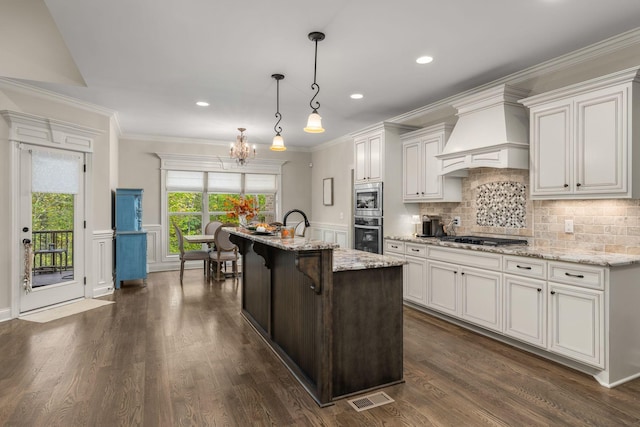 kitchen featuring a breakfast bar, hanging light fixtures, custom range hood, white cabinets, and a center island with sink